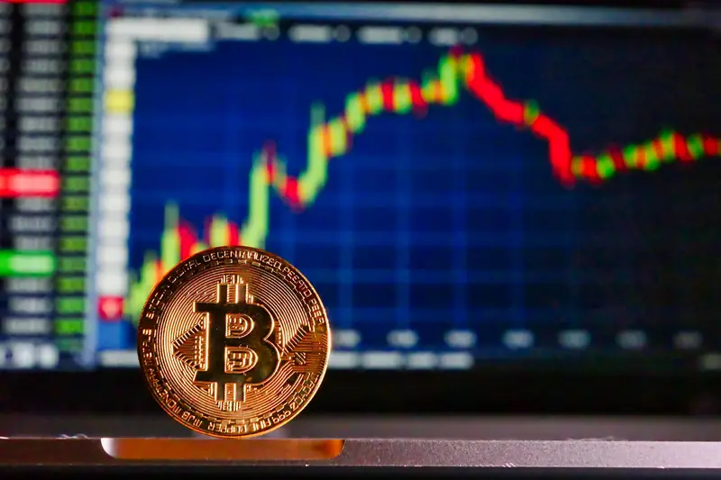 Koin Bitcoin di depan layar grafik perdagangan, ilustrasi bursa kripto seperti Indodax