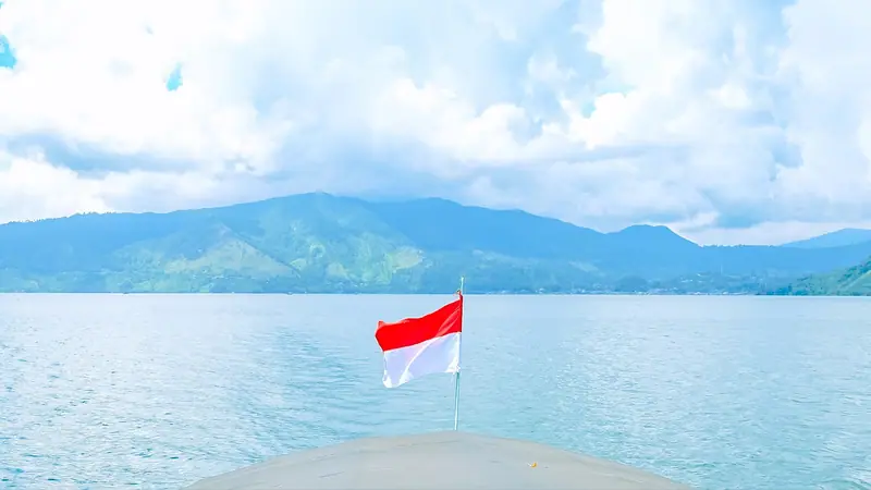 Danau dan laut dengan bendera kecil Indonesia di depan pegunungan, gambaran lanskap Bali